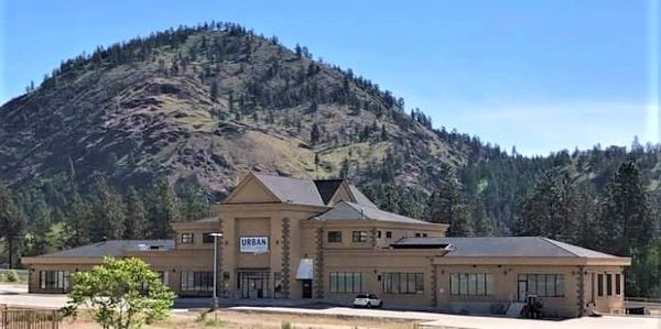 A long and tall gray building with a big mountain covered in trees behind at Urban Distillary