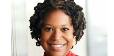 A woman smiling warmly with curly hair and a red top.