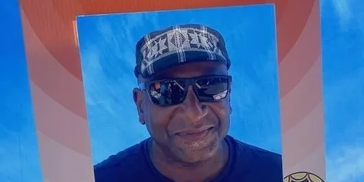 Man wearing sunglasses and a patterned cap smiling.