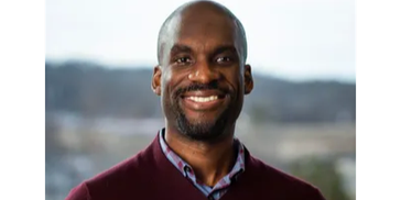 Smiling man in a maroon sweater with blurred outdoor background.
