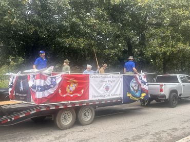 A parade float honoring veterans with banners and flags towed by a pickup truck.