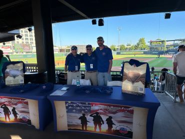 Three men at military appreciation booth in a stadium.