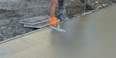 Worker smoothing freshly poured concrete with a trowel outdoors.