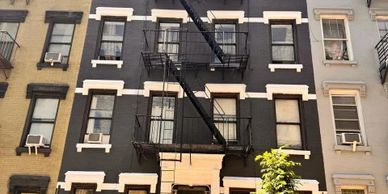 A row of urban buildings with fire escapes and window air conditioners.