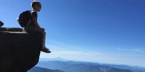 Boy sitting on edge of cliff with backpack.