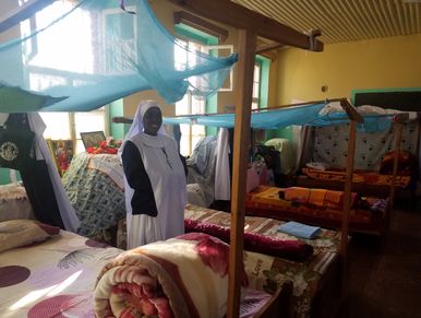 A nun standing in a dormitory with beds covered by mosquito nets.