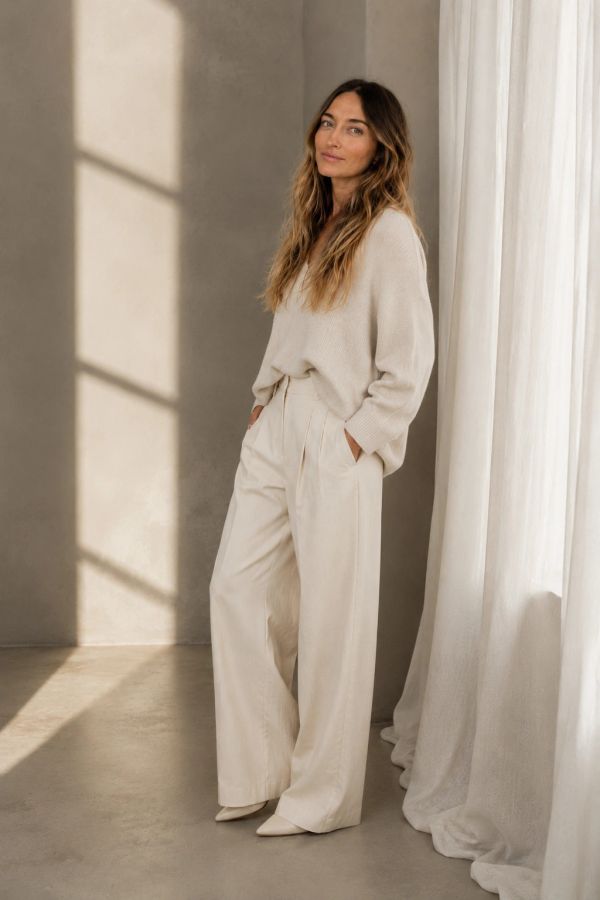 Woman wearing a beige sweater and wide-legged trousers.