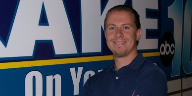 A man smiles standing in front of a news station sign.
