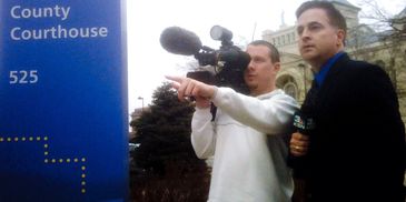 A reporter and cameraman outside a county courthouse preparing for a news segment.