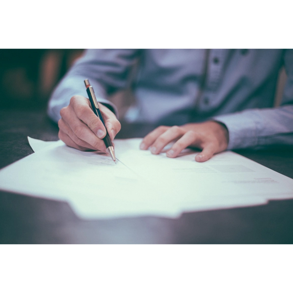 Person writing on documents with a pen at a desk.
