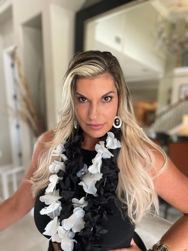 Woman with long blonde hair wearing a black and white floral lei.