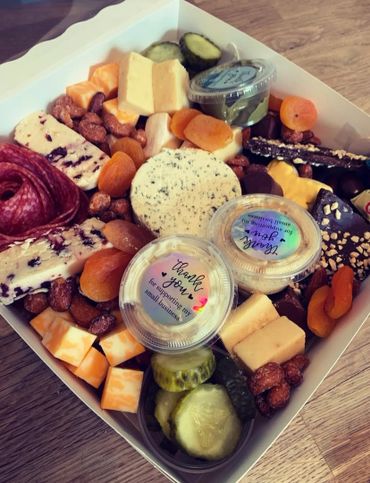 A gourmet charcuterie box with cheeses, nuts, dried apricots, pickles, and salami.
