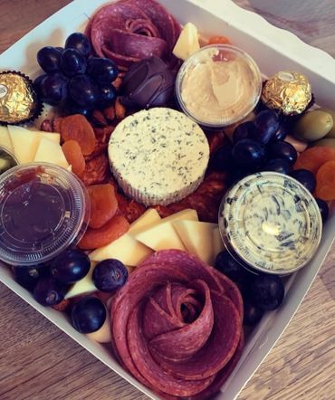 A gourmet charcuterie box with cheese, grapes, salami, chocolates, and dips.