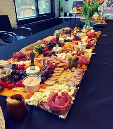 A long charcuterie board with meats, cheeses, fruits, and dips on a black tablecloth.