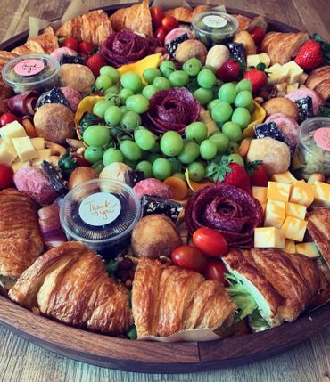 A vibrant platter with croissants, grapes, cheese, and various fruits and meats.