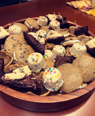 A wooden platter filled with assorted cookies, brownies, and frosted treats.