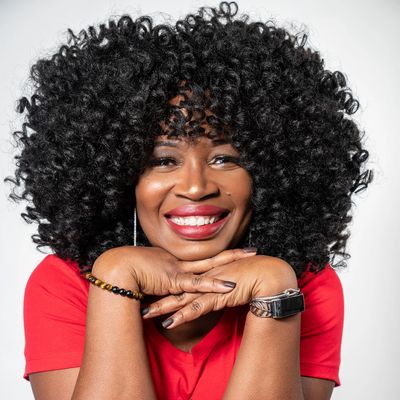 Smiling woman with voluminous curly hair and red lipstick, wearing a red top.