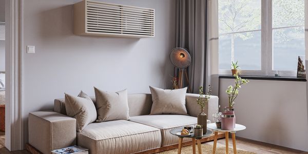 Cozy beige sofa with cushions, small tables, and a floor lamp in a bright, minimalist living room.