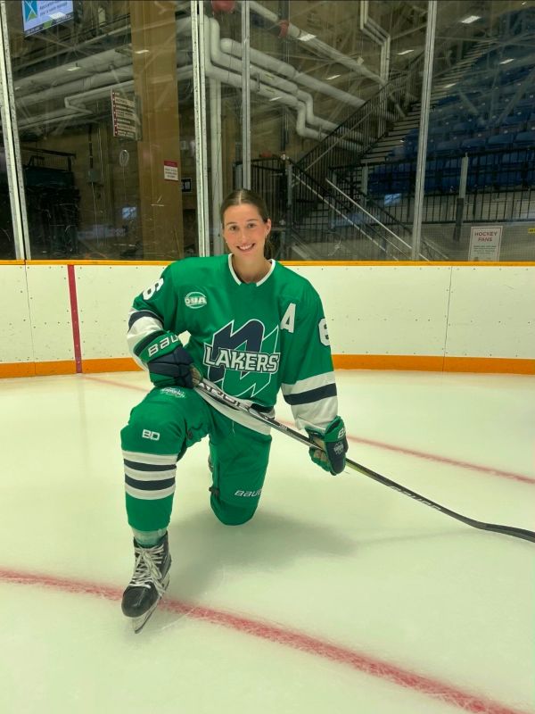 Female hockey player kneeling on ice rink with stick.