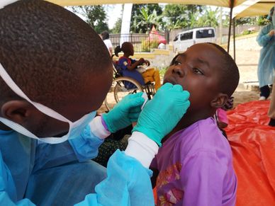 A healthcare worker in protective gear tests a child's throat.