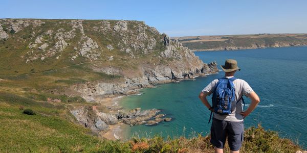 A man with a backpack overlooking a rocky coastal cliff and blue sea.