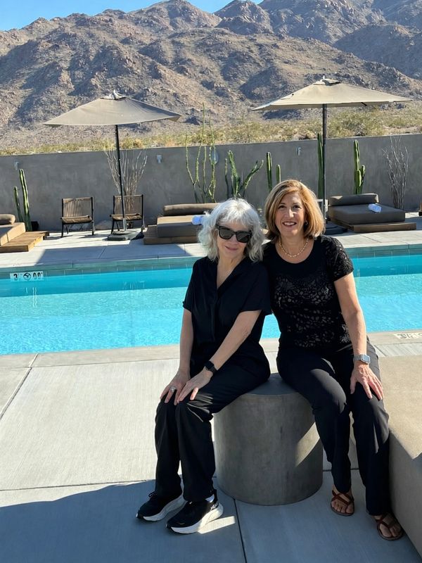 Two women sitting by a pool with a mountain backdrop on a sunny day.