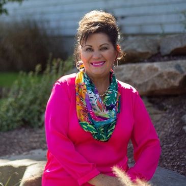 Smiling woman in bright pink outfit with colorful scarf outdoors.