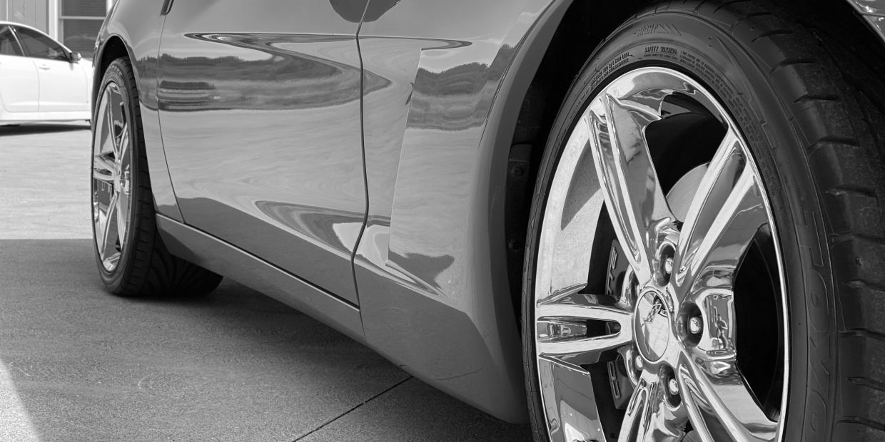 Close-up of a shiny car wheel and body on a driveway.