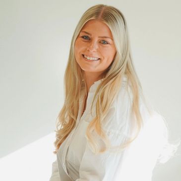 Smiling woman with long blonde hair in a white shirt against a light background.