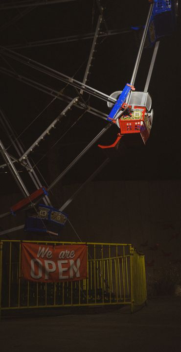 Ferris wheel ride at night with a 'We are OPEN' sign and yellow fence.