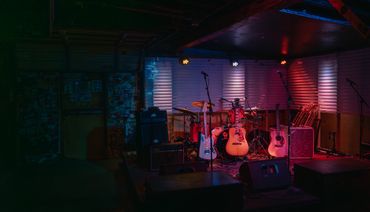 Dimly lit stage with guitars, drums, and amplifiers ready for a live music performance.