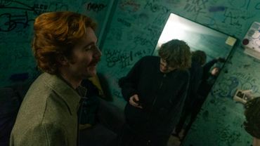 Two young men in a dimly lit room covered with graffiti.