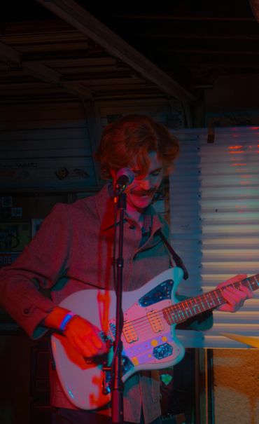 Man playing an electric guitar and singing into a microphone under colorful lighting.