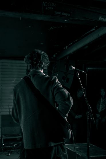 Musician performing on stage with guitar and microphone in dim lighting.