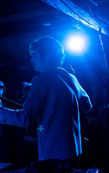 Musician performing on stage with blue lighting and audience watching.
