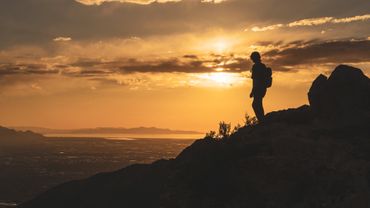 Silhouette of a hiker on a rocky mountain at sunset.