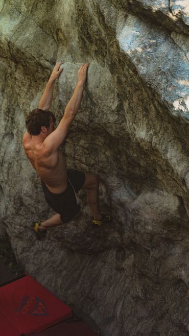 Shirtless man bouldering on a rocky surface with climbing shoes.