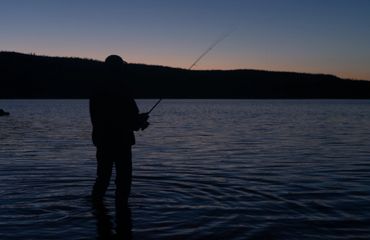 Silhouette of a person fishing in a lake at dusk.
