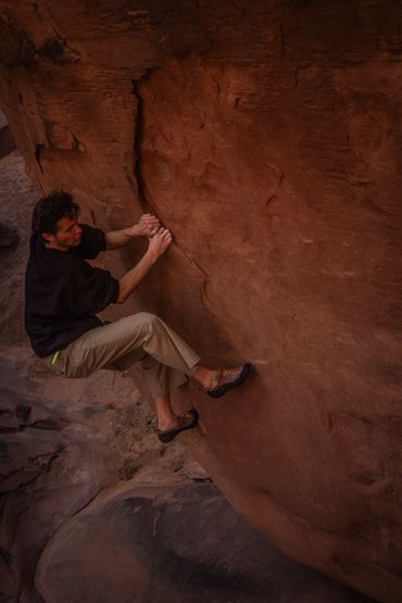 A man bouldering on a steep reddish rock face.