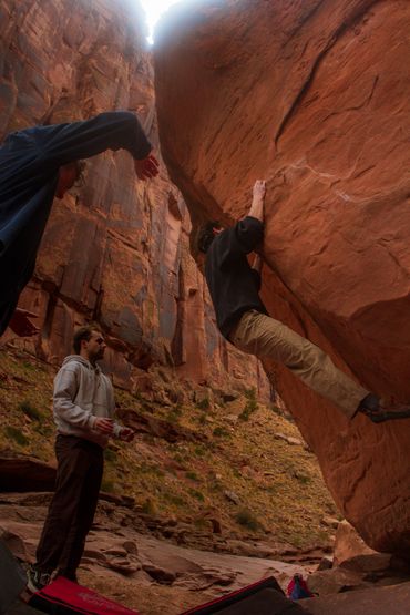 Three men rock climbing in a canyon with one climbing and two spotting.