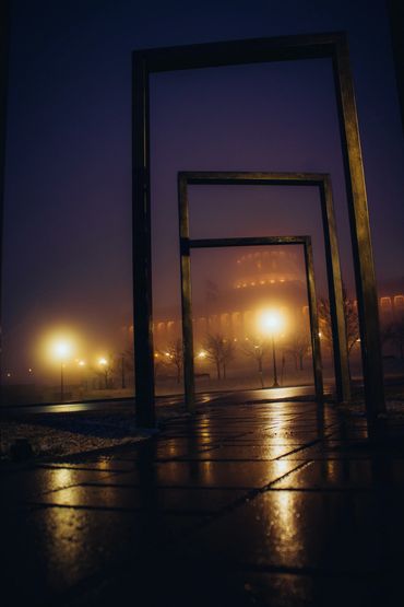 Metal frames on a wet path with glowing street lamps in foggy night.