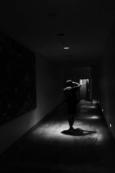 A person stands alone in a dimly lit corridor with stairs ahead.
