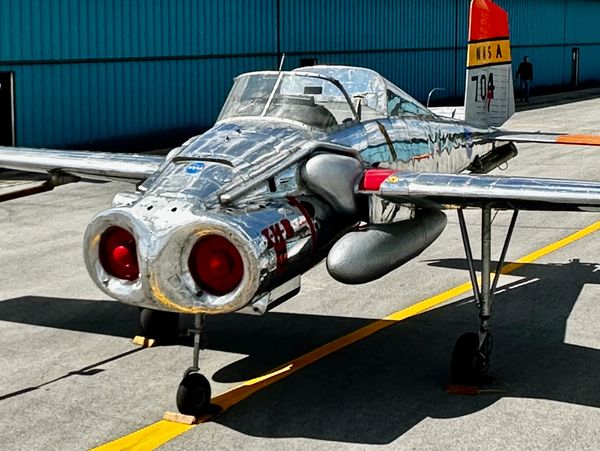 Shiny metallic NASA aircraft with twin red engine exhausts on runway.