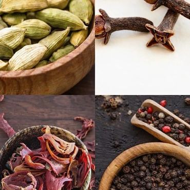 Close-up of various spices including cardamom, cloves, mace, and peppercorns in wooden bowls.