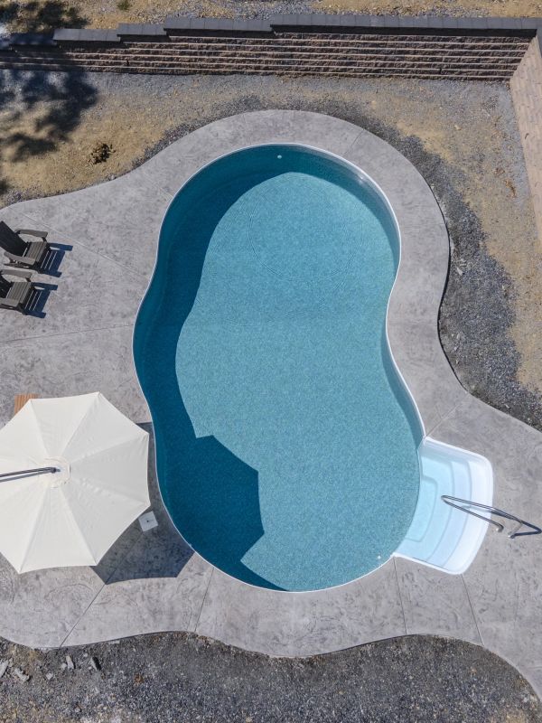 A uniquely shaped swimming pool with a white umbrella and lounge chairs.