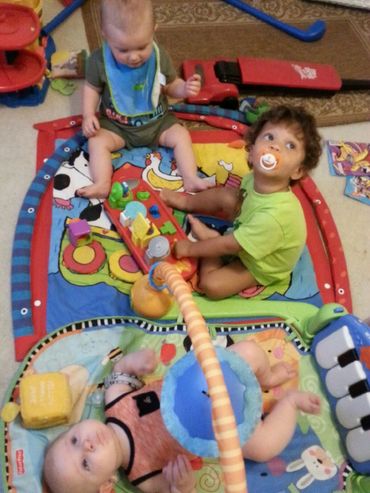 Pic 11
Two daycare toddlers sit on a multi-color blue and red activity mat playing. 
