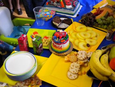 Pic 19
Birthday table with blue tablecloth, white plates, birthday cake, sliced pineapple, fruits.