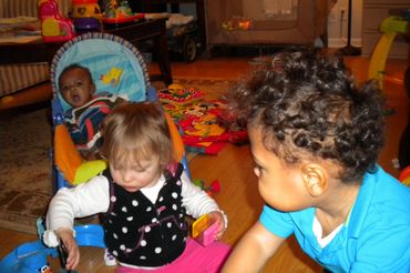 Pic 7.
Boy and girl plays on the floor. Baby in a blue and orange rocker looks on in the background.