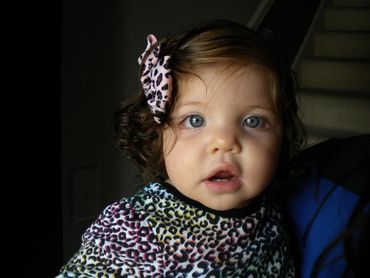 Pic 18.
Toddler with piercing blue eyes, wearing an animal print bow and top, staring at the camera.