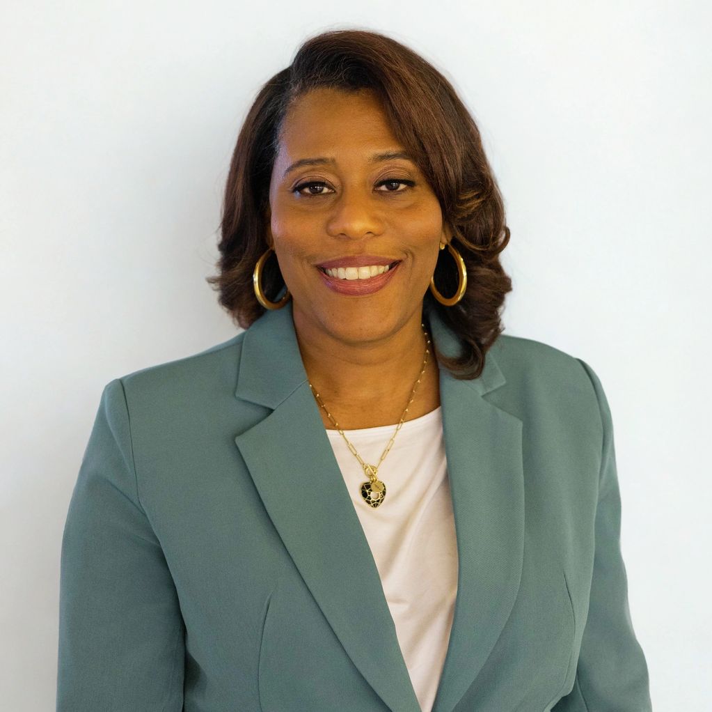 Professional woman smiling in a teal blazer and gold jewelry.